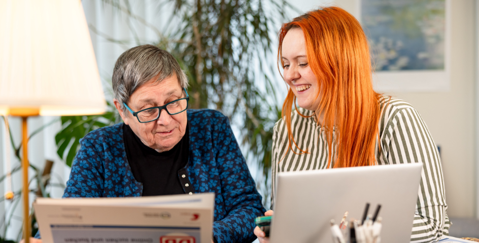 Eine ältere sitzt neben einer jüngeren Frau, beide haben einen Laptop und eine Broschüre vor sich. Fotograf: Jörg Farys